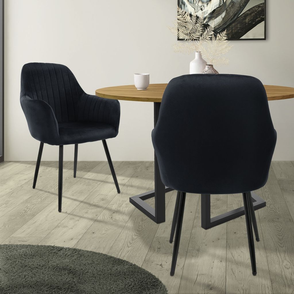Two black velvet chairs at a round wooden dining table.
