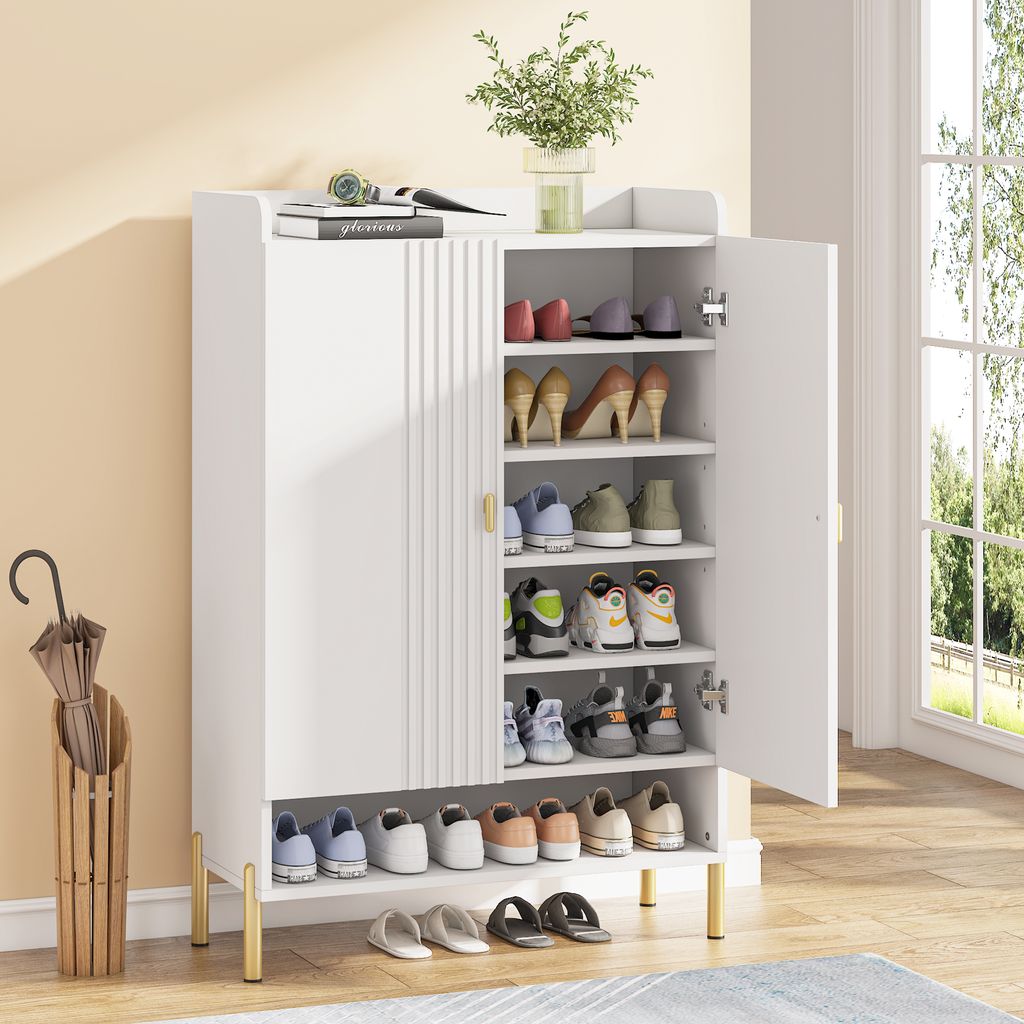 A white shoe cabinet with multiple shelves filled with shoes, placed in a room with a window and an umbrella stand.