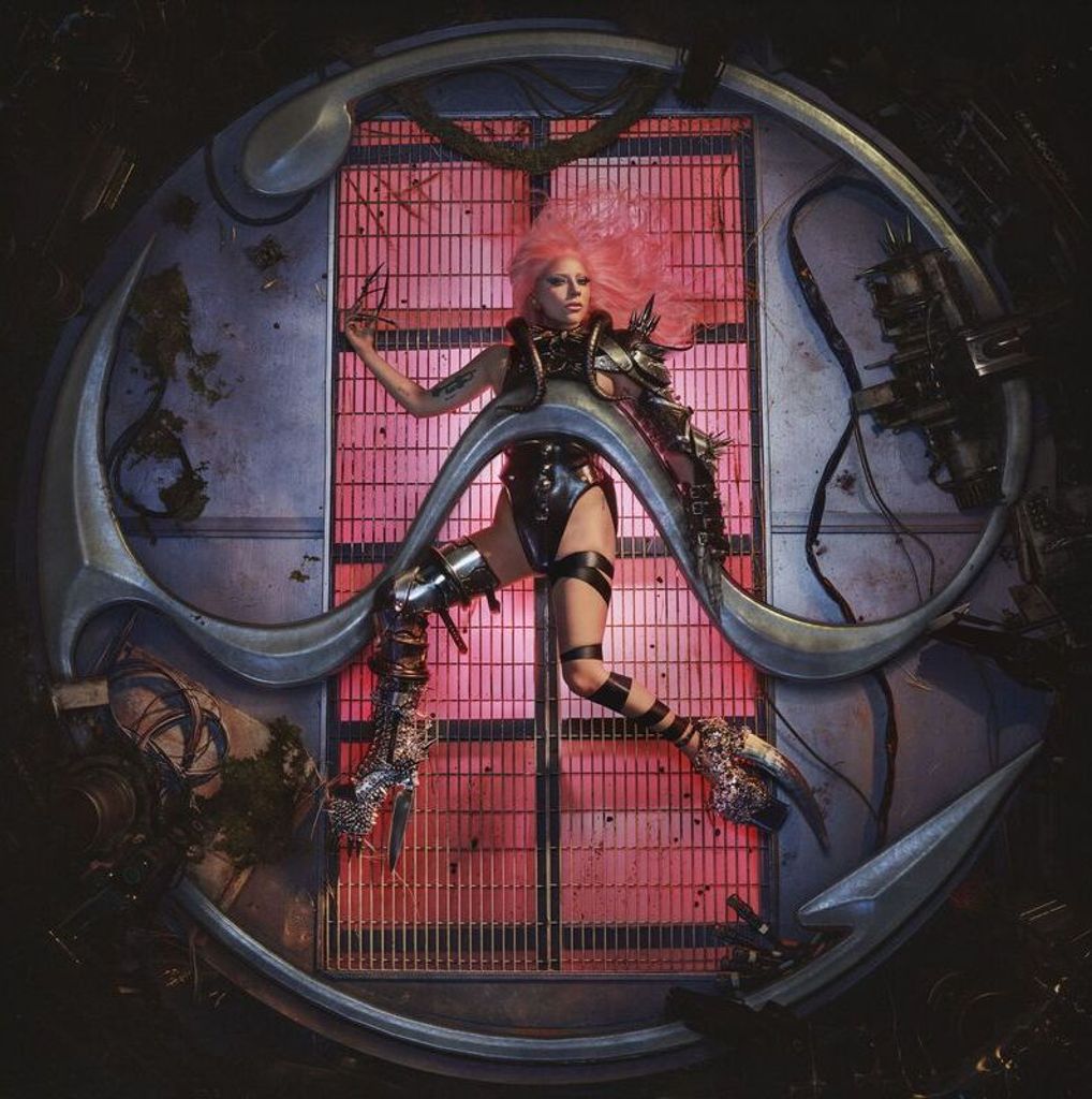 A woman with pink hair in a futuristic outfit is suspended within a circular metallic structure against a red background.