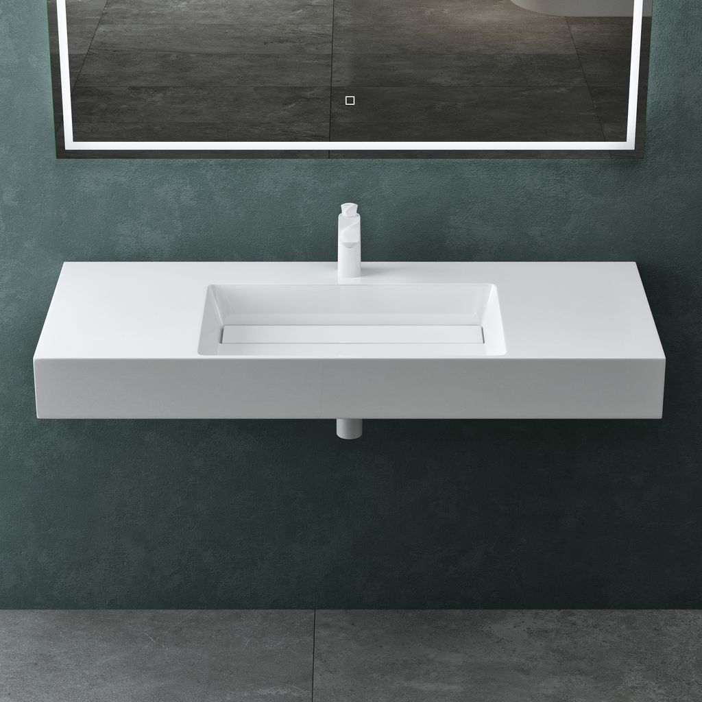 A modern white wall-mounted sink with a minimalist faucet and a large illuminated mirror above it, set against a dark teal wall and gray tiled floor.