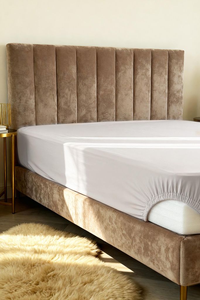 A fitted sheet is shown on a bed with a plush rug in the foreground.