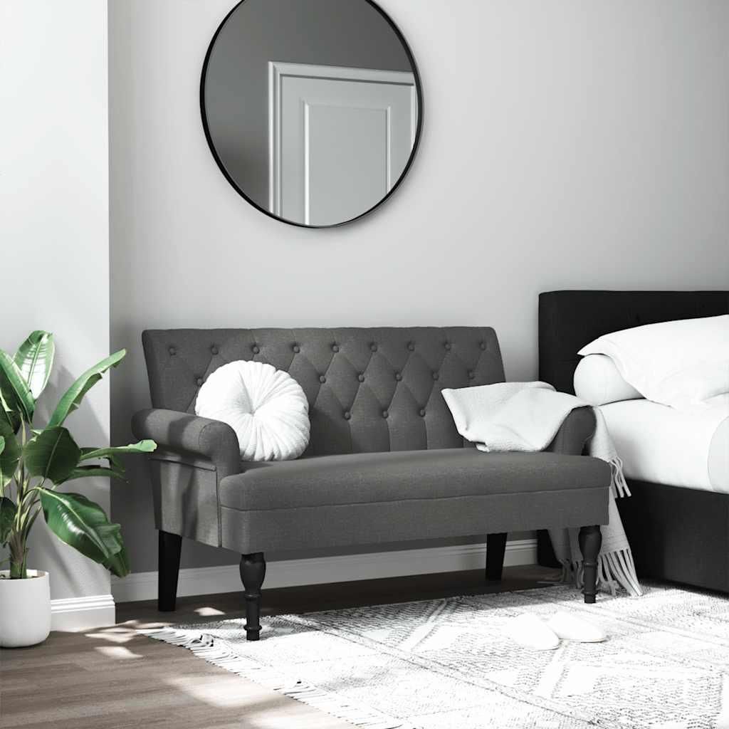 A dark gray tufted bench with a white round pillow and a white throw blanket is placed in a bedroom setting next to a bed.