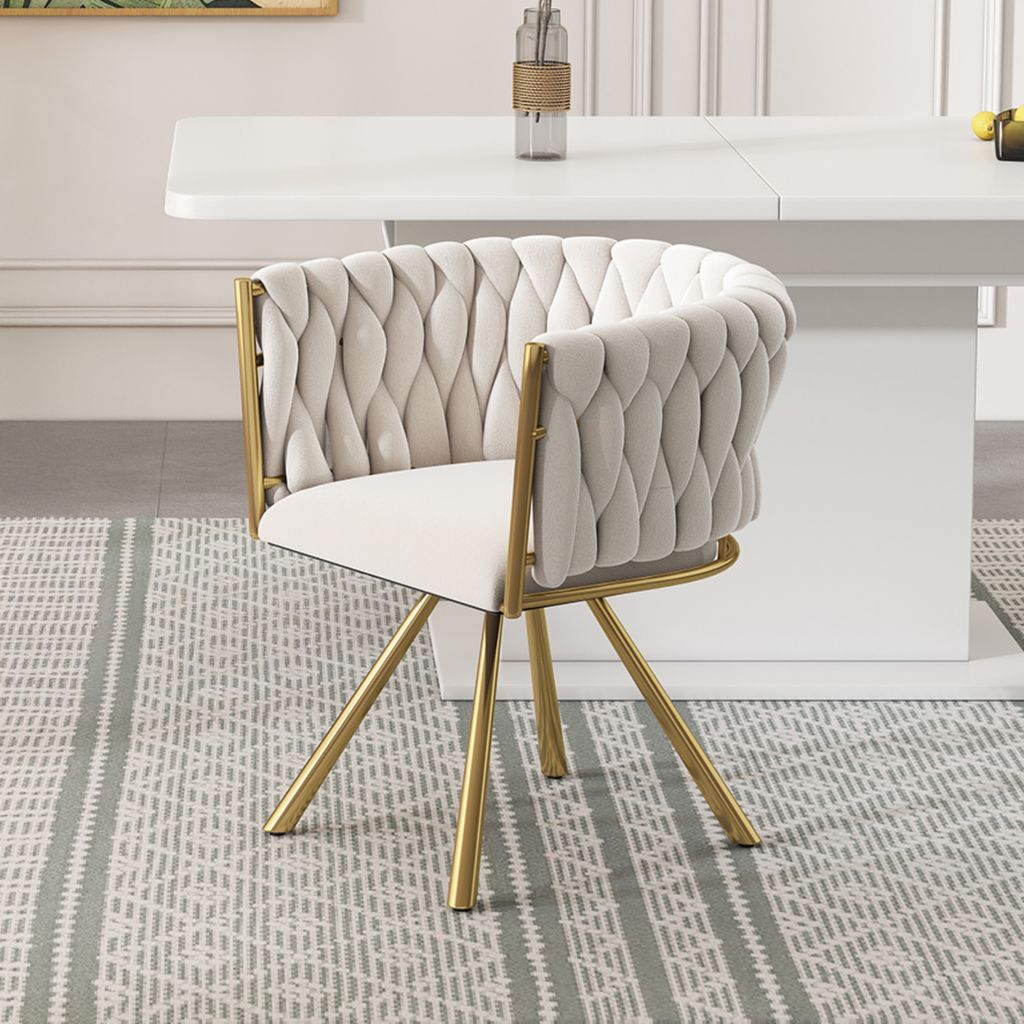 A beige upholstered chair with gold legs sits on a patterned rug in front of a white table.