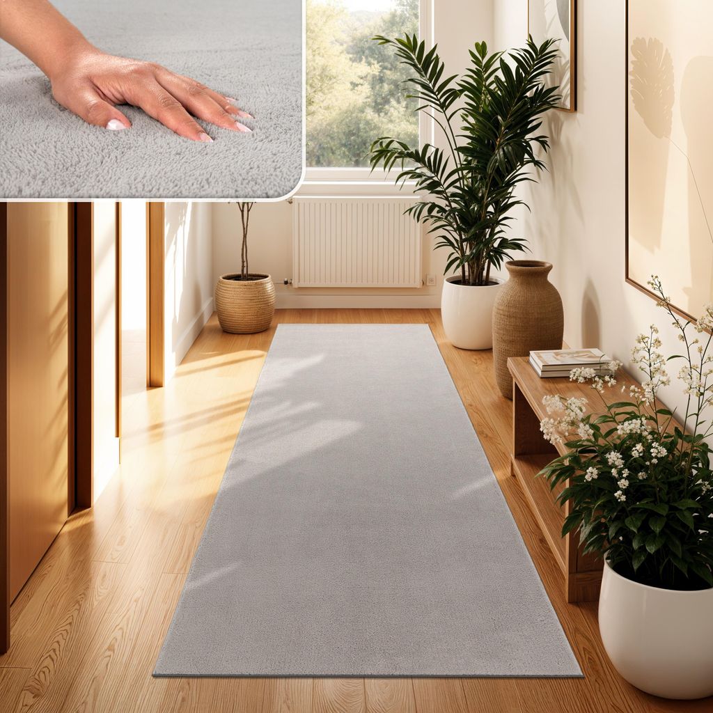 A hallway with a long, light gray runner rug on a wooden floor, decorated with plants and a bench.
