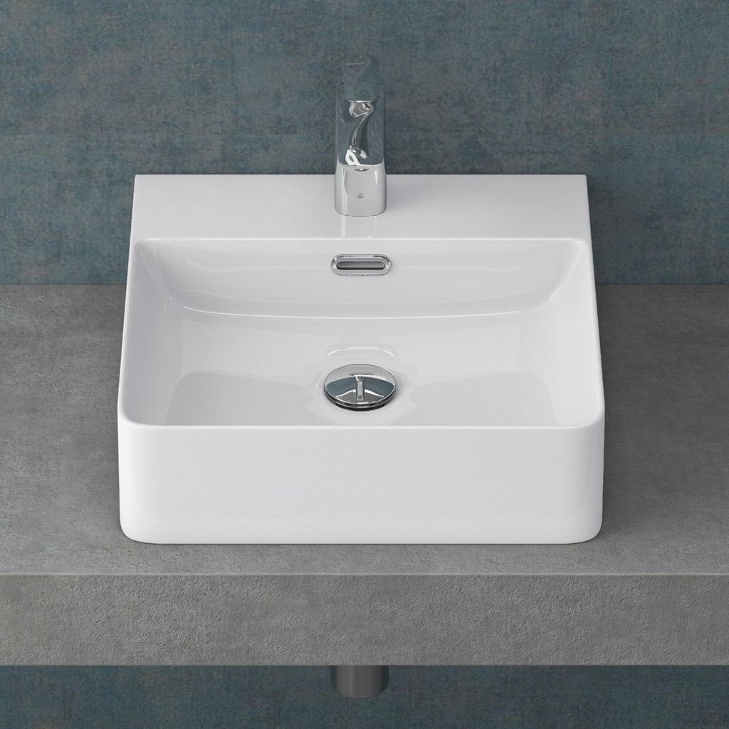 A white ceramic sink with a chrome faucet and drain, placed on a gray countertop against a blue textured wall.