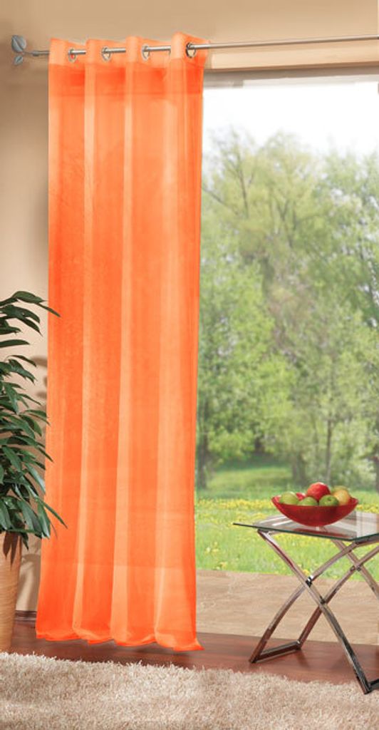 An orange sheer curtain hangs in front of a window with a view of trees and grass. A small table with a bowl of fruit is visible.