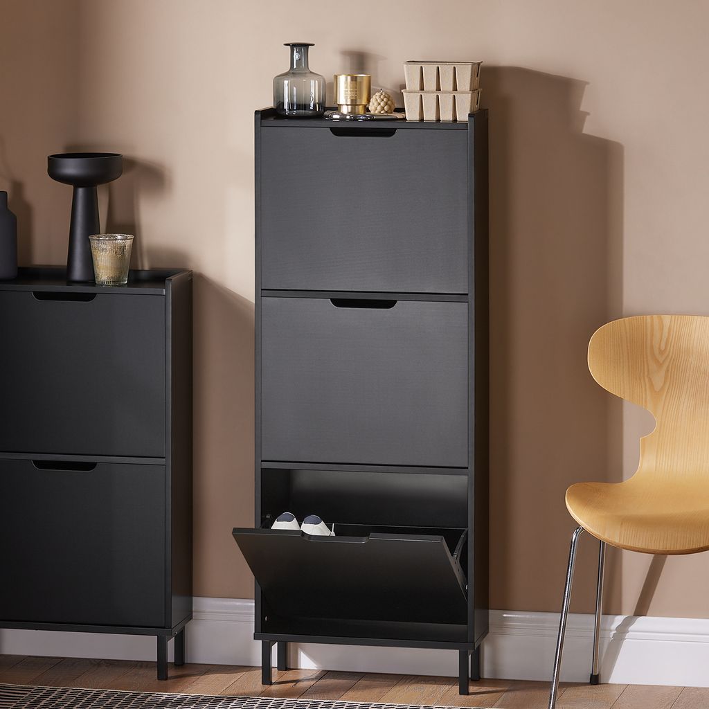 A black shoe cabinet with multiple flip-down compartments, placed next to another similar cabinet and a wooden chair.