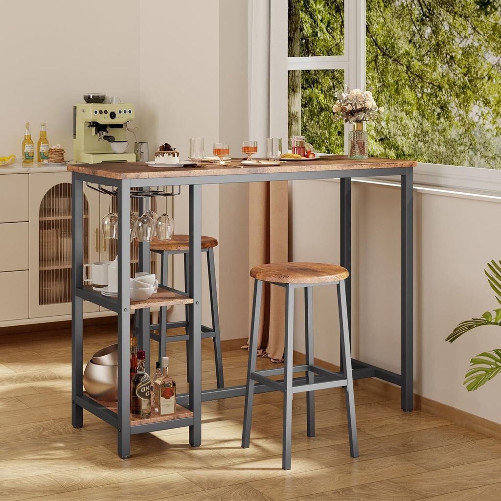 A bar table set with two stools and shelves, placed near a window with greenery outside. The table is set with glasses and a small cake.