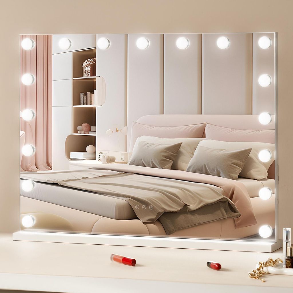 A vanity mirror with lights is placed on a dresser in front of a bed.
