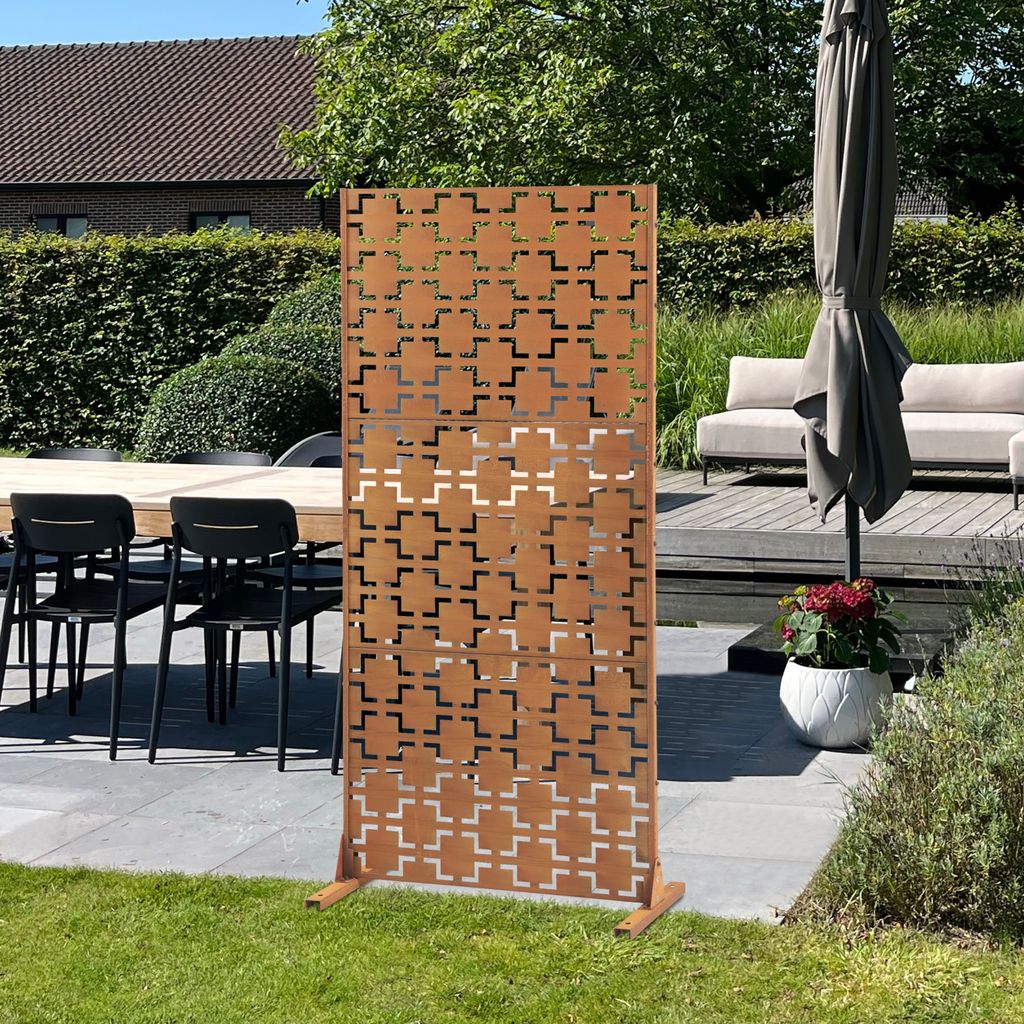 A decorative screen is placed on a patio next to outdoor furniture and plants.
