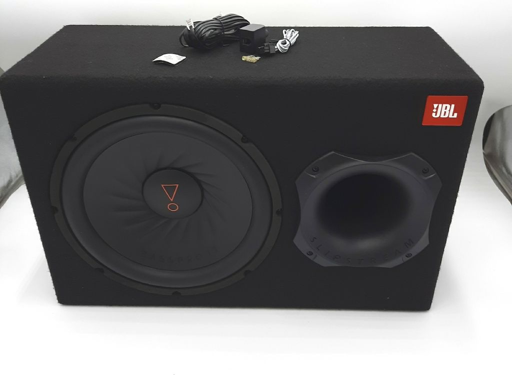 A black JBL subwoofer in a box, with cables and accessories on top.