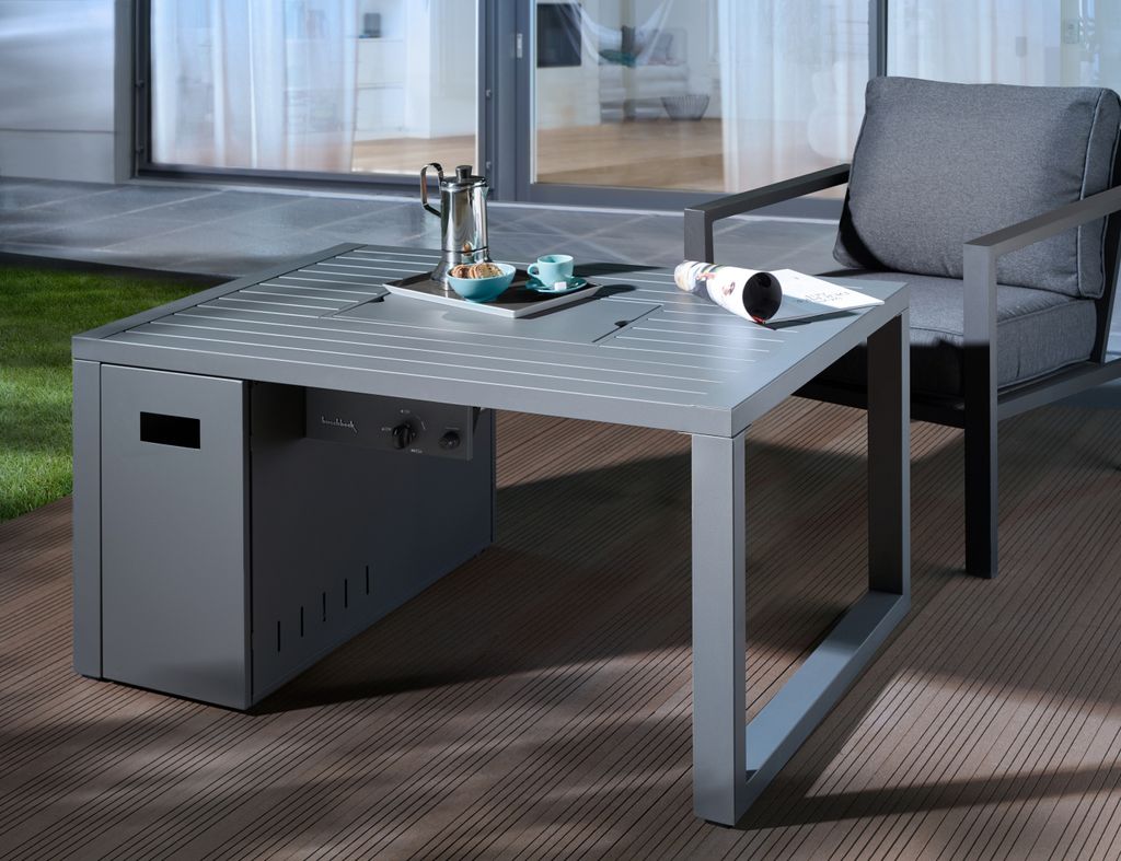 A grey outdoor lounge table with a built-in fire pit, set on a wooden deck next to a grey armchair.