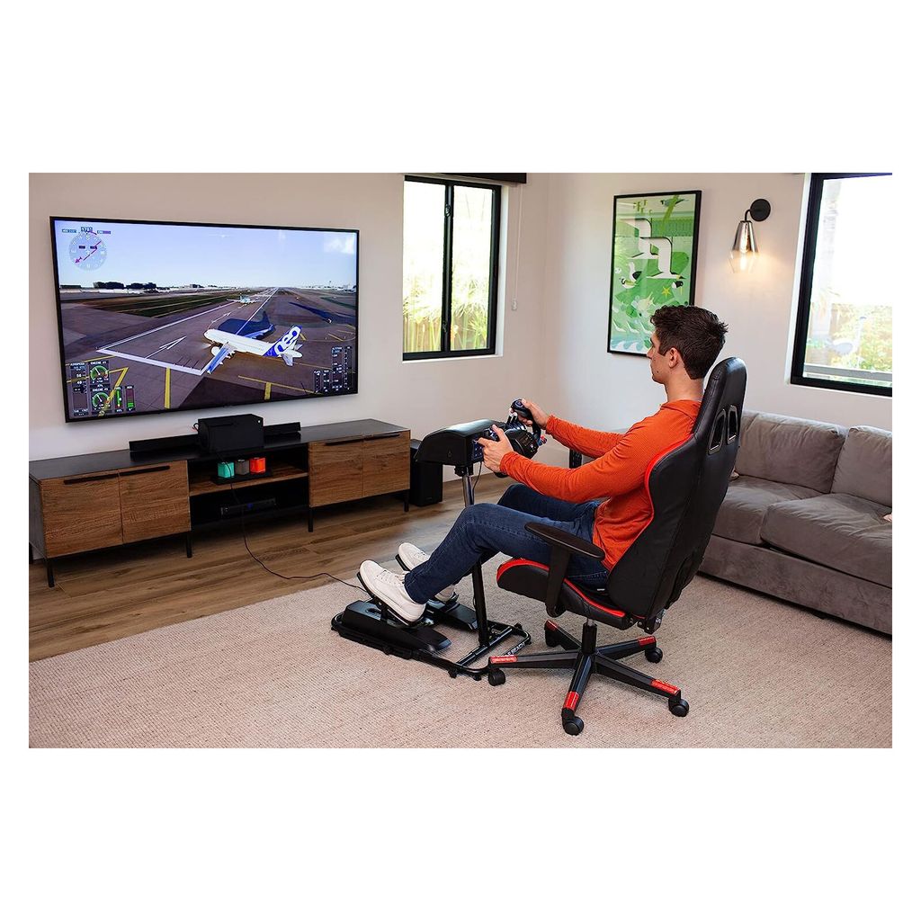 A man is playing a flight simulator game using a racing wheel and pedals setup in a living room.