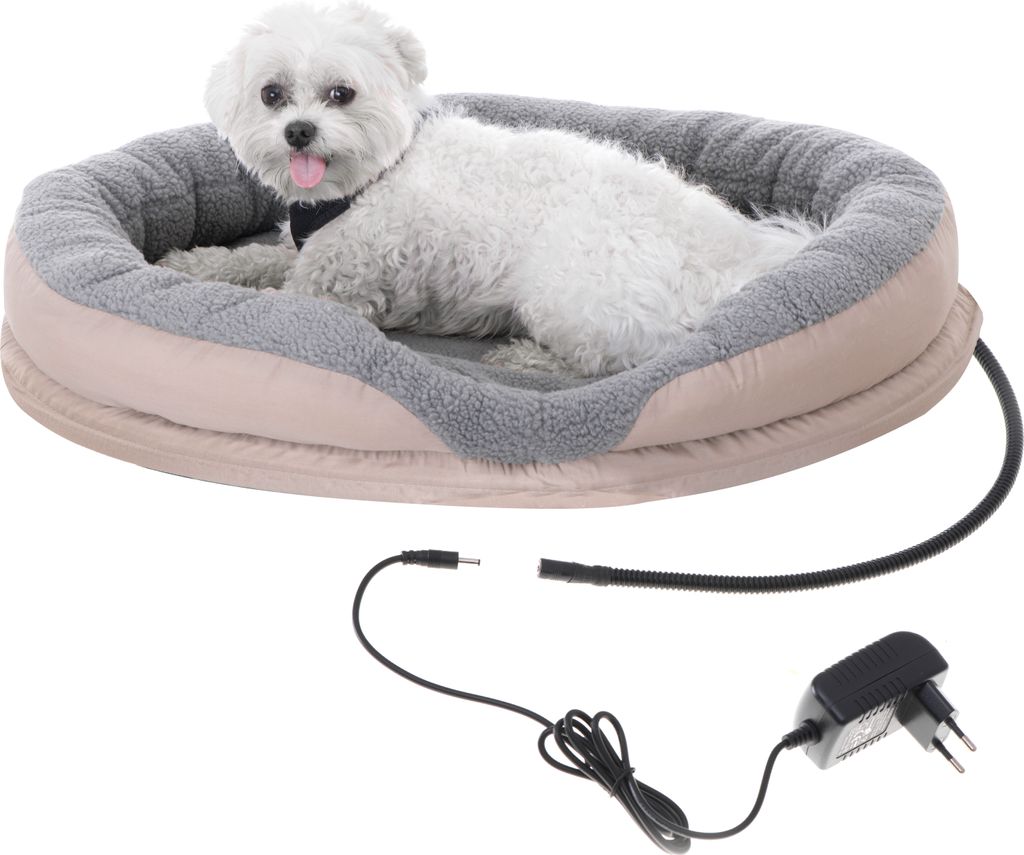 A small white dog is lying in a heated pet bed with a power adapter and cord visible in the foreground.