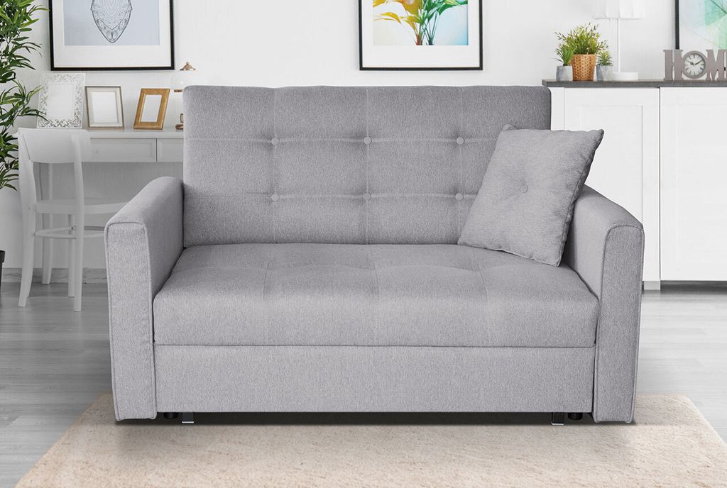 A gray sofa is shown in a well-lit room with a desk and pictures in the background.