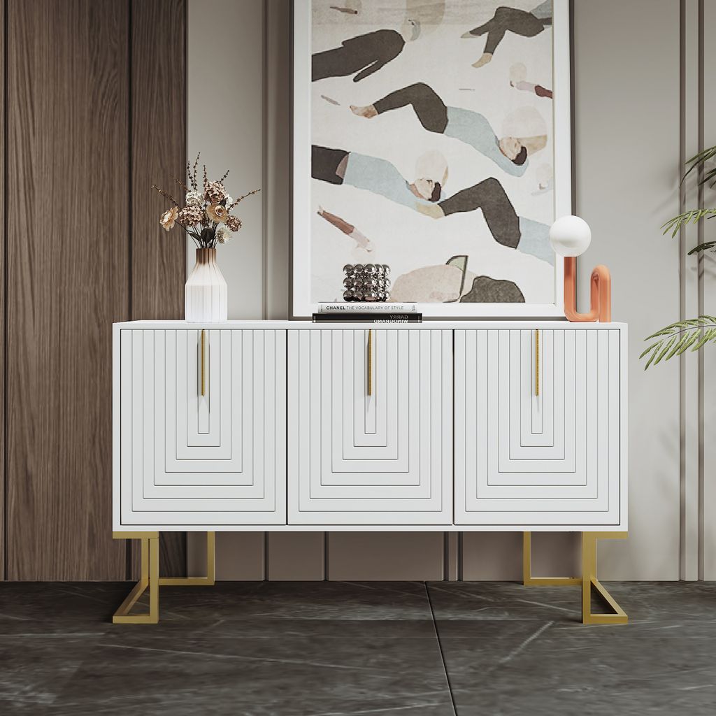 A white sideboard with gold legs and handles is displayed in a room with a wooden wall and a large abstract painting above it.