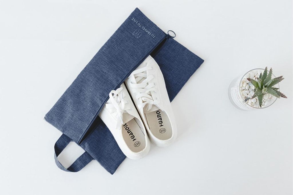 A pair of white sneakers is placed inside a blue denim organizer bag, which is laid open on a white surface. A small potted succulent plant is visible to the right.