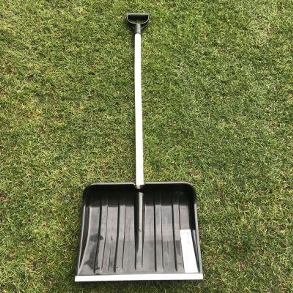 A black shovel with a white handle lies on a green grassy lawn.
