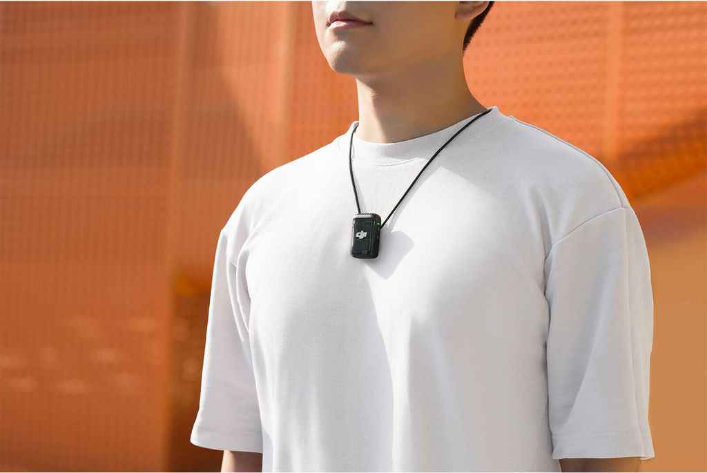 A person wearing a white t-shirt and a black DJI Mic 2 transmitter necklace against an orange and light gray background.