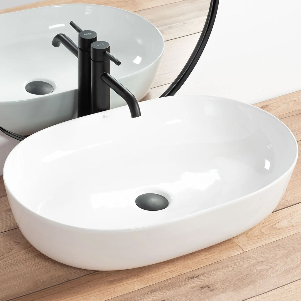 A white oval countertop sink with a black faucet is shown on a wooden surface.