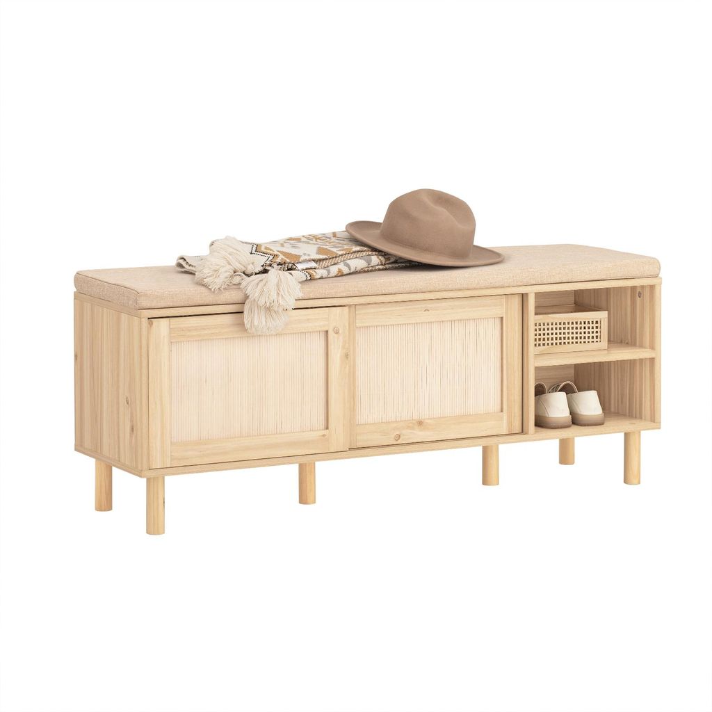 A wooden shoe bench with a cushioned seat, featuring sliding doors and open shelving for shoe storage. A hat and scarf are placed on the seat.