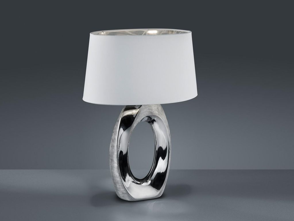 A table lamp with a silver base and a white shade is displayed against a plain gray background.