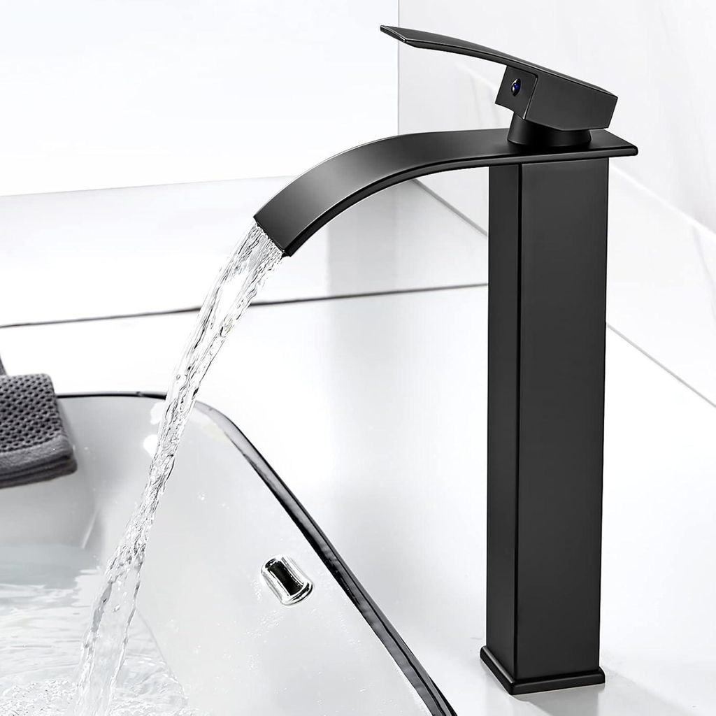 A black waterfall faucet in a modern bathroom, with water flowing into a sink.