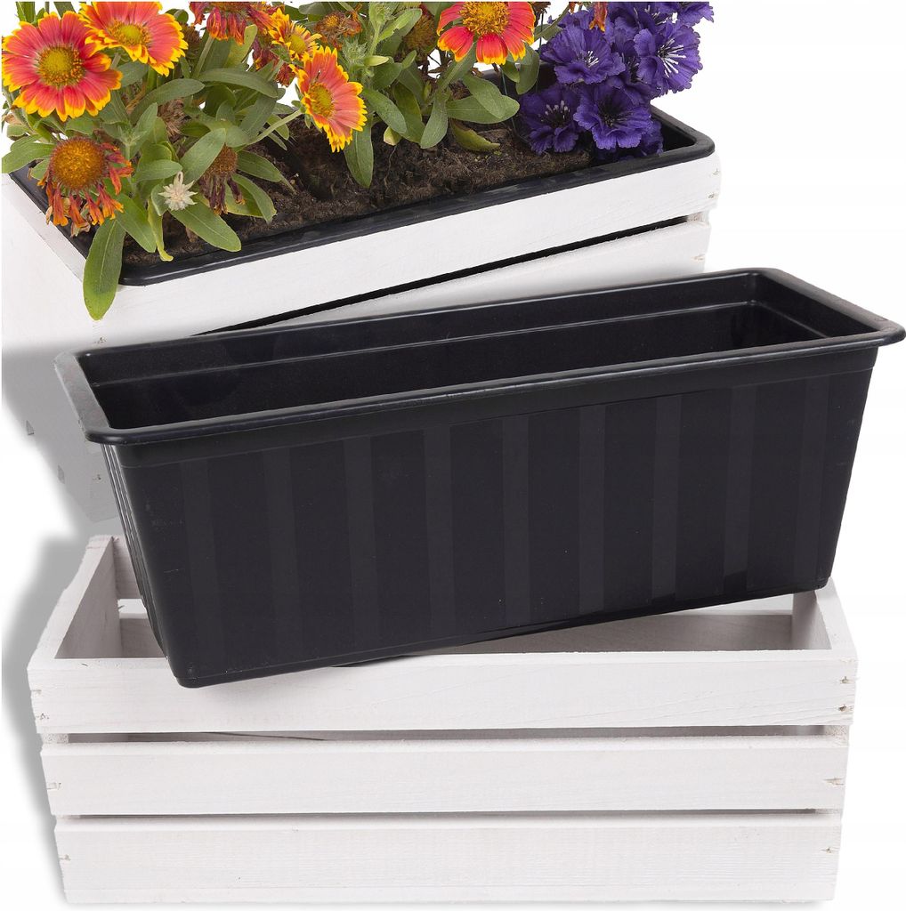 A black plastic planter box is placed on top of a white wooden crate, with flowers in a white planter box visible in the background.