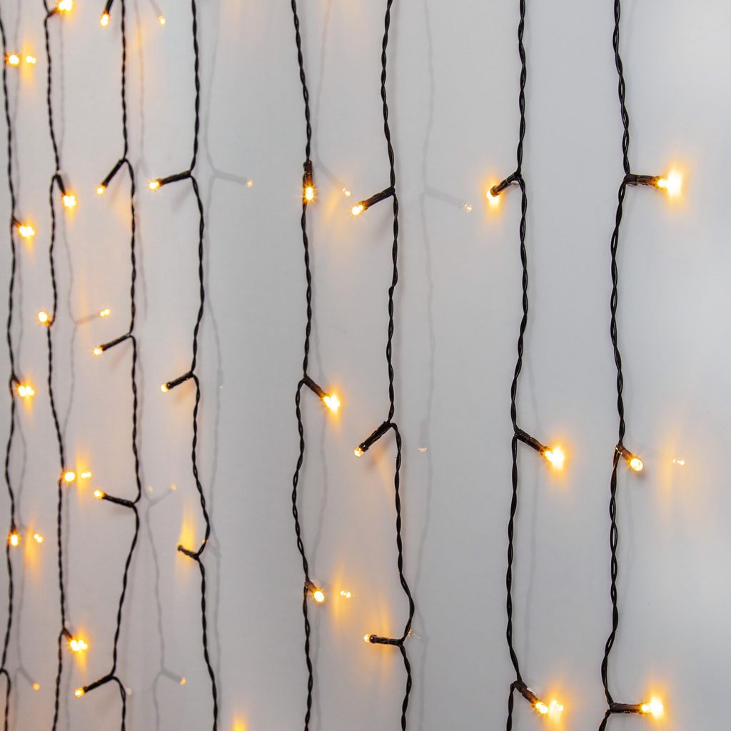 A close-up view of multiple strands of LED string lights hanging vertically against a light gray wall.
