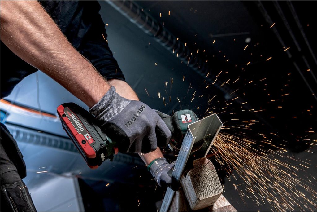 A person is using a cordless angle grinder to cut metal, with sparks flying.