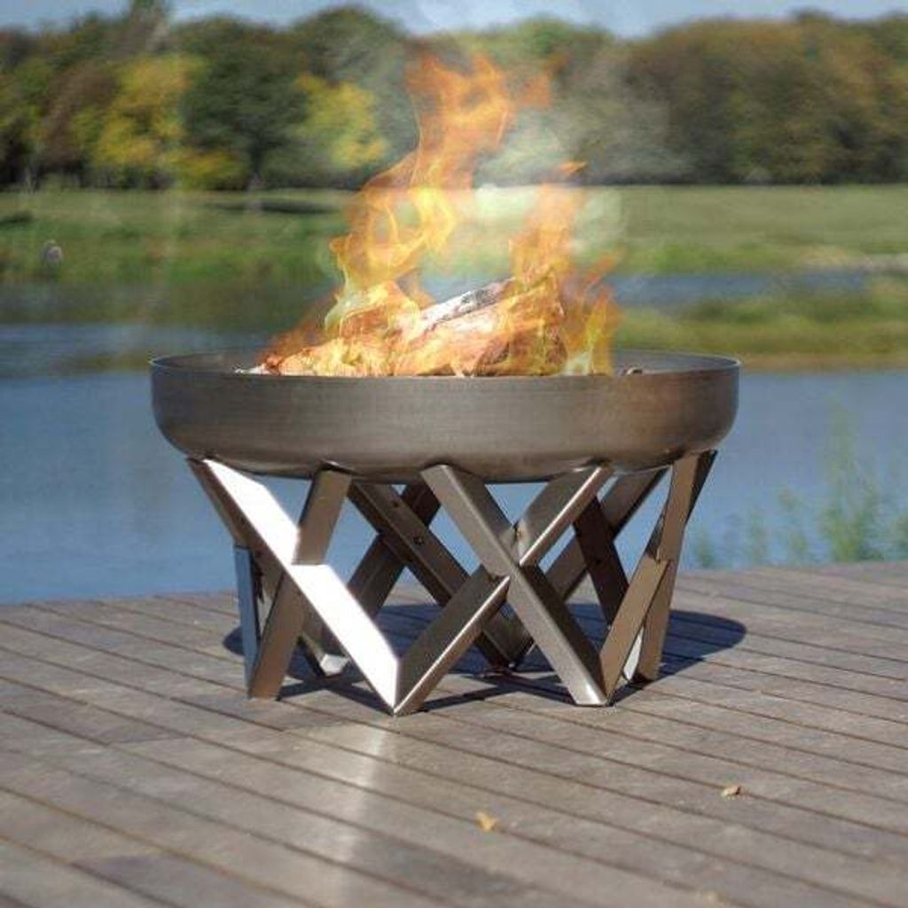 A fire pit on a wooden deck next to a body of water with trees in the background.