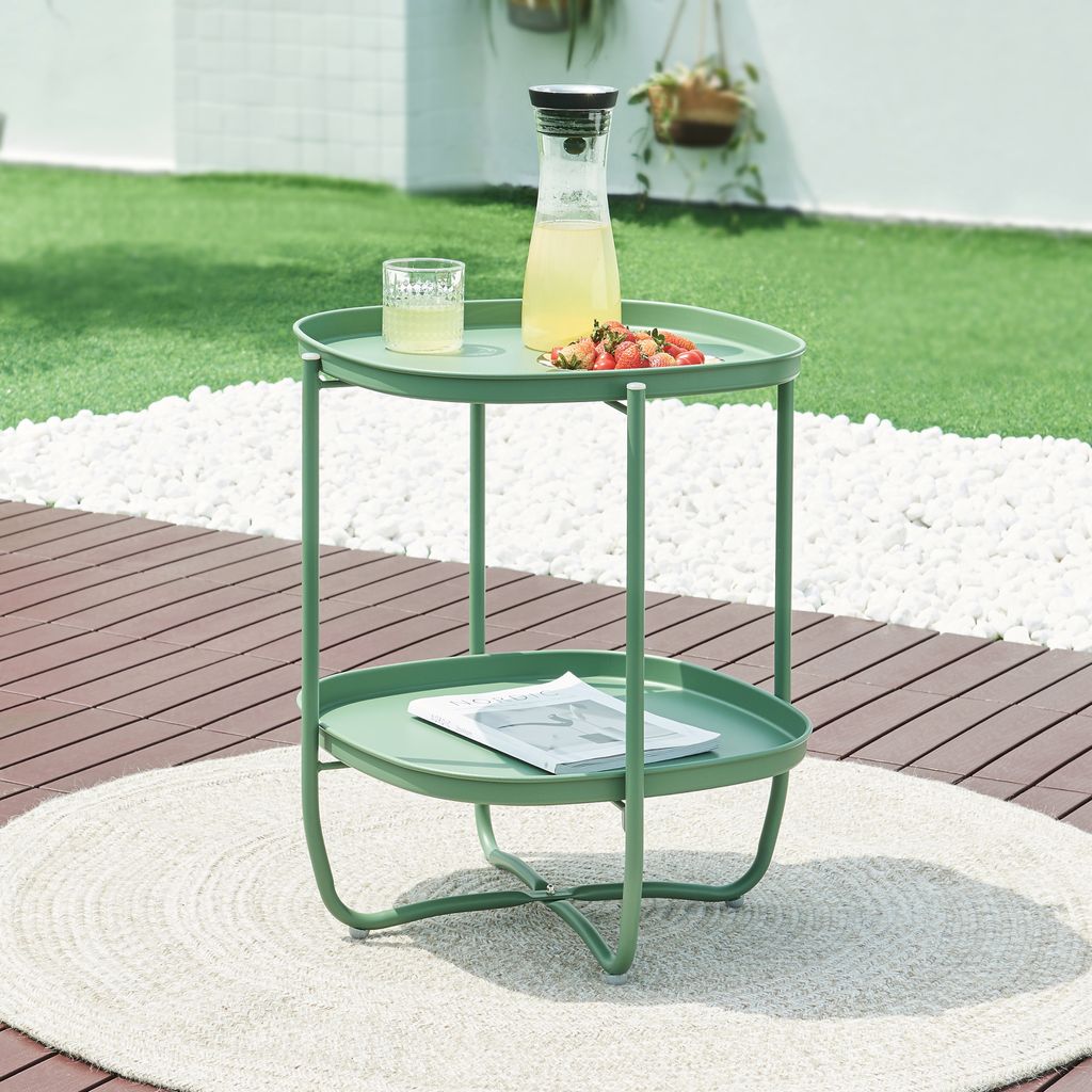 A green side table with drinks and fruit on it, placed on a patio.