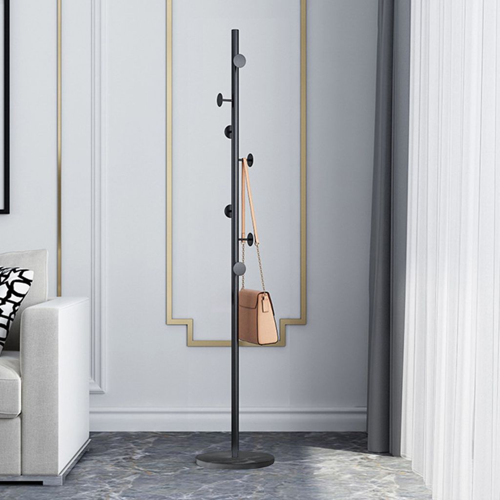 A black coat rack with a tan handbag hanging on it, placed in a room with a white sofa and a decorative wall.
