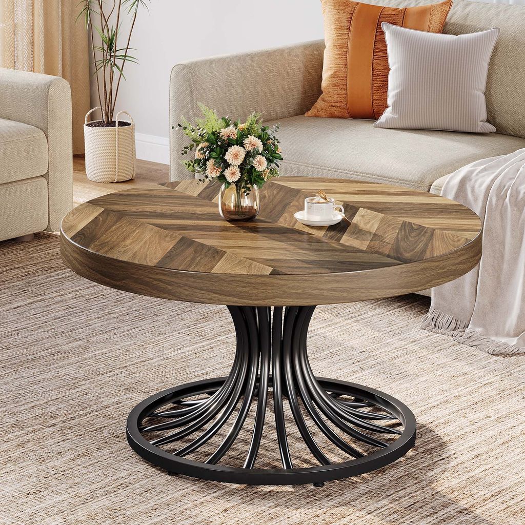 A round wooden coffee table with a metal base is placed in a living room setting next to a sofa.