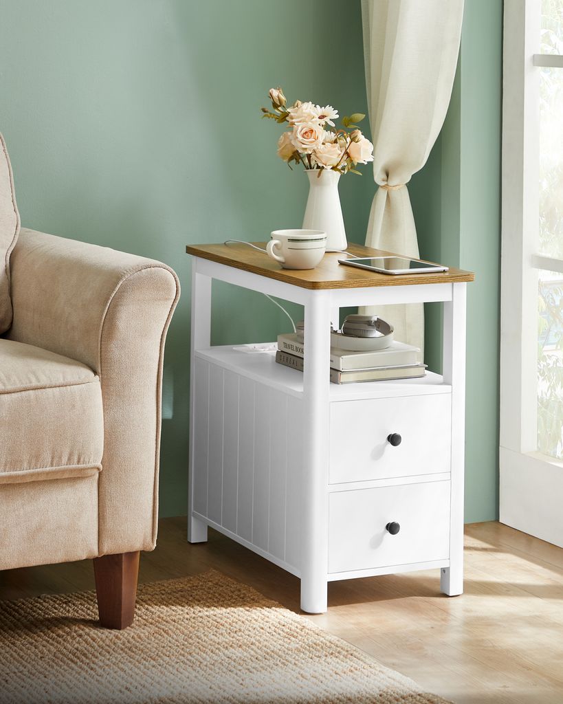A bedside table with a cup and flowers next to a chair.
