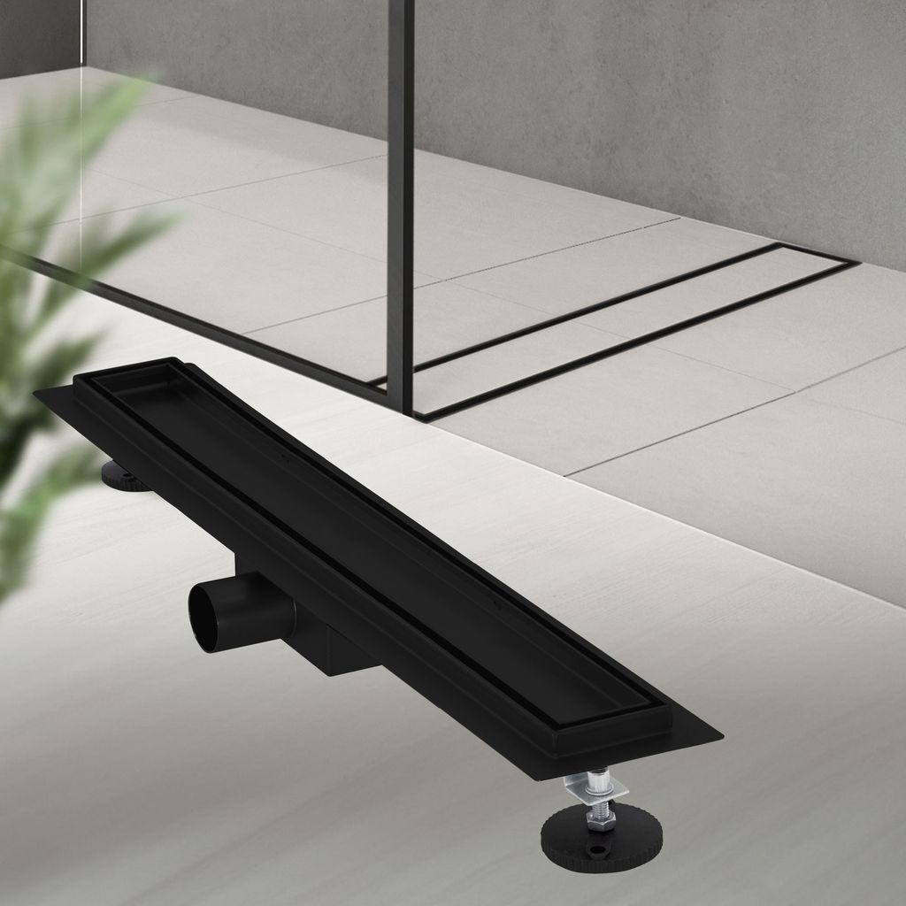 A black linear shower drain is shown on a tiled floor, with a glass shower enclosure in the background.