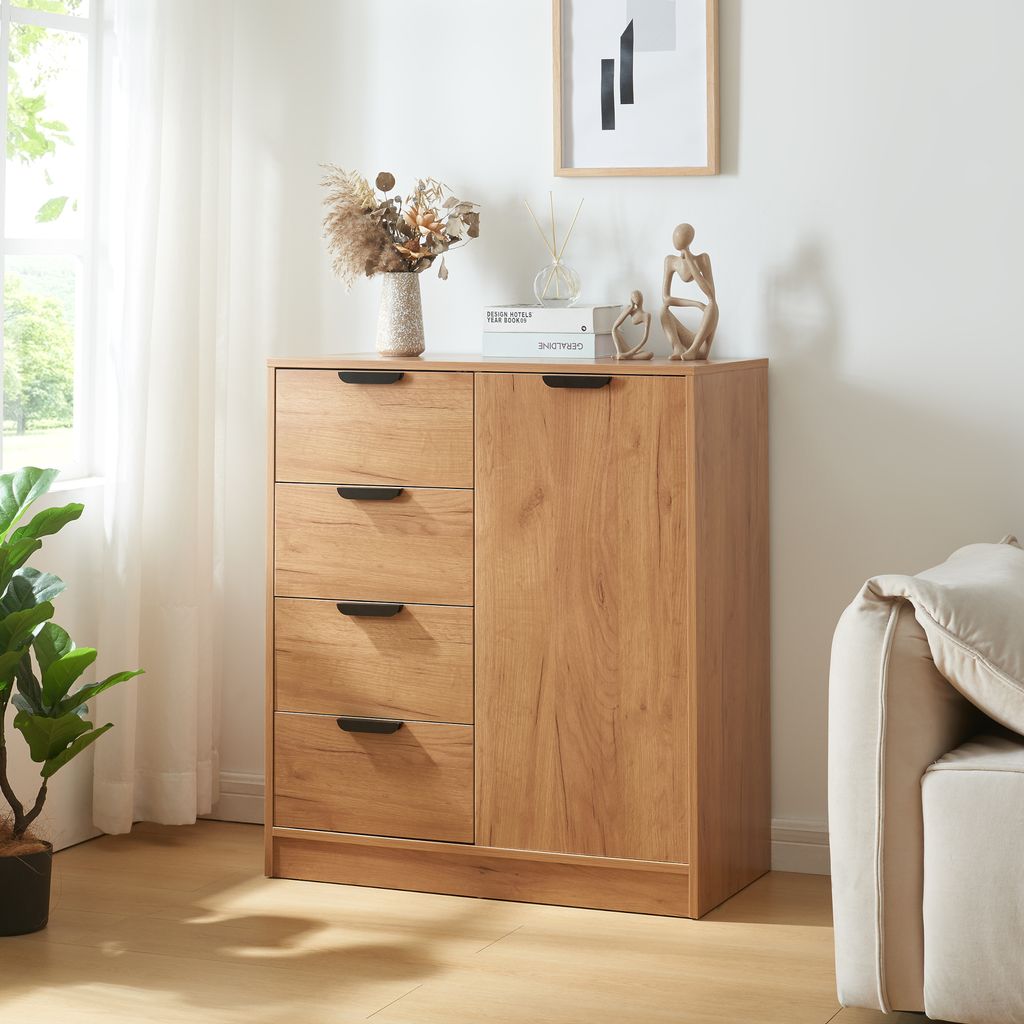 A wooden cabinet with drawers and a door, decorated with a vase of dried flowers and small sculptures, placed in a room with a sofa and a window with curtains.