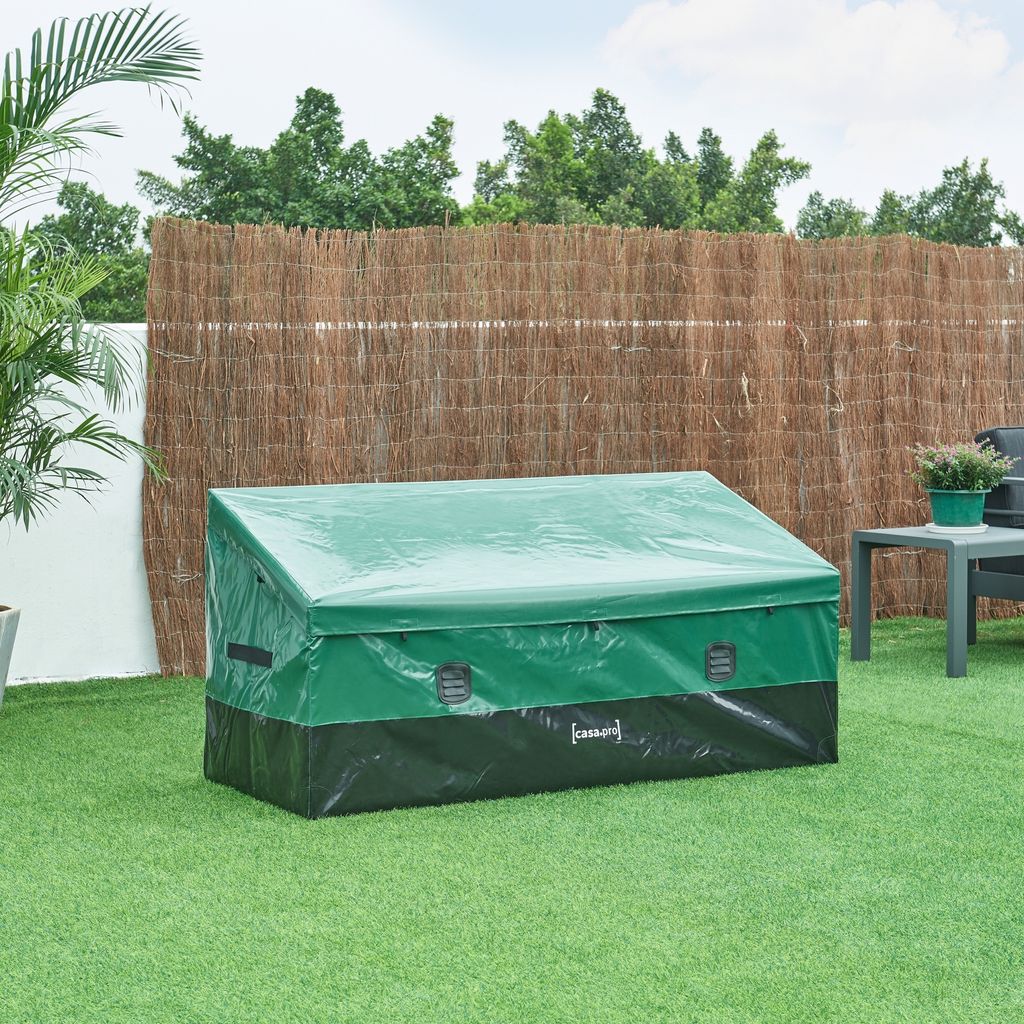 An outdoor scene with a covered storage box on artificial grass, a bamboo fence in the background, and a small table with a potted plant to the right.