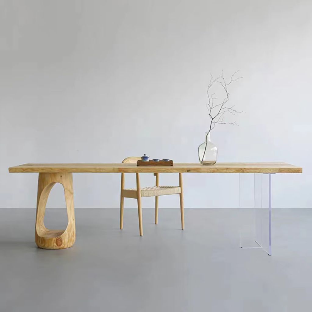 A modern wooden dining table with unique carved legs and clear acrylic legs, set against a plain wall.