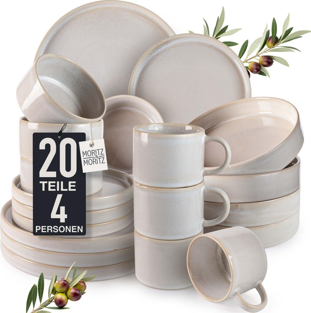 A collection of ceramic dishes and mugs, arranged in stacks and piles, with olive branches and olives in the foreground and upper right.