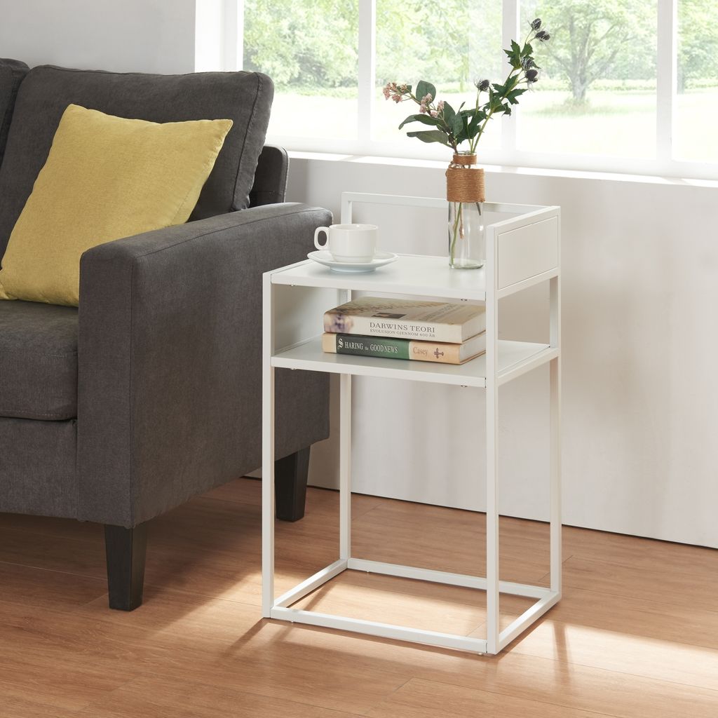 A white side table with books and a vase of flowers next to a gray sofa with a yellow pillow.