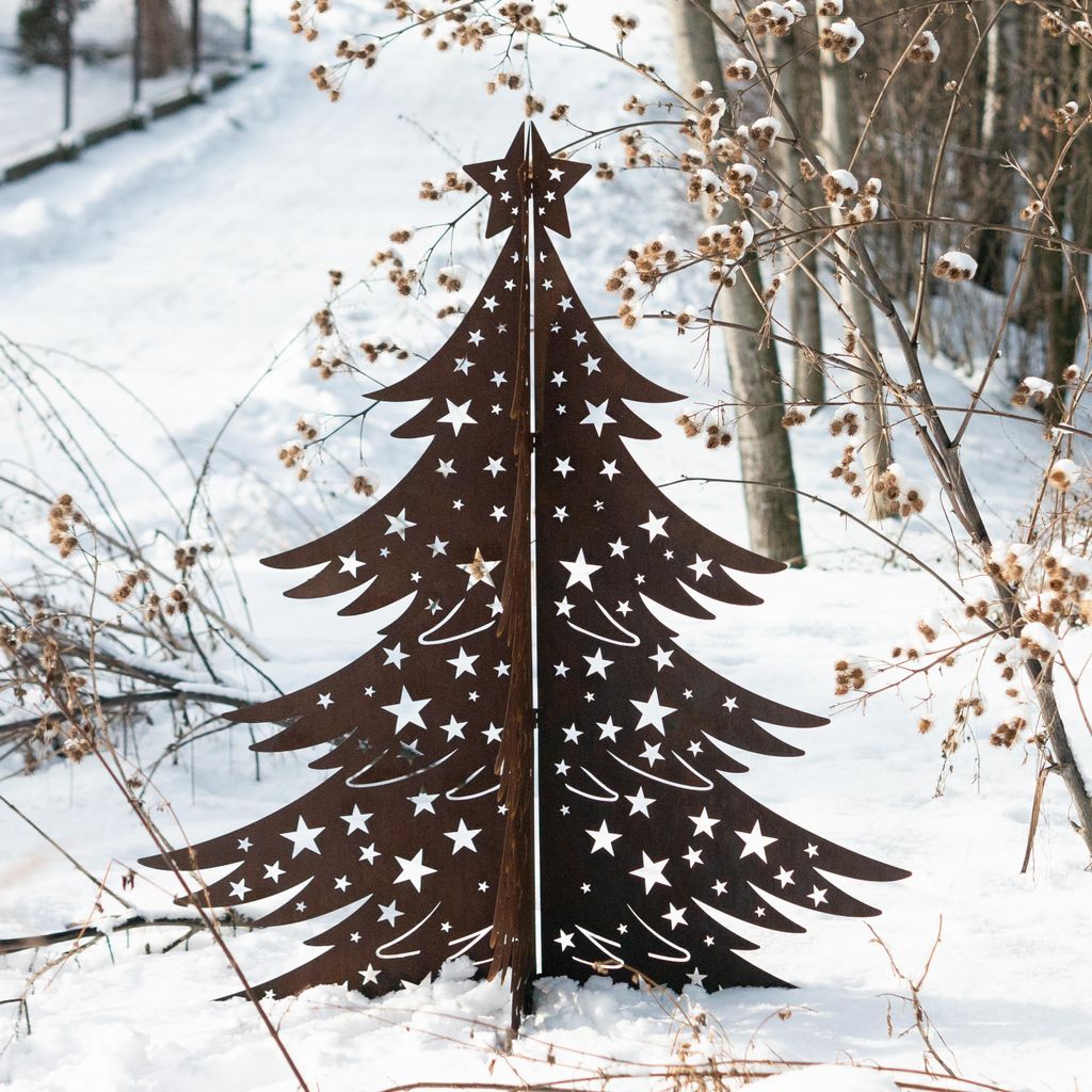 A metal Christmas tree decoration with star cutouts stands in the snow, surrounded by bare branches and dried seed pods.