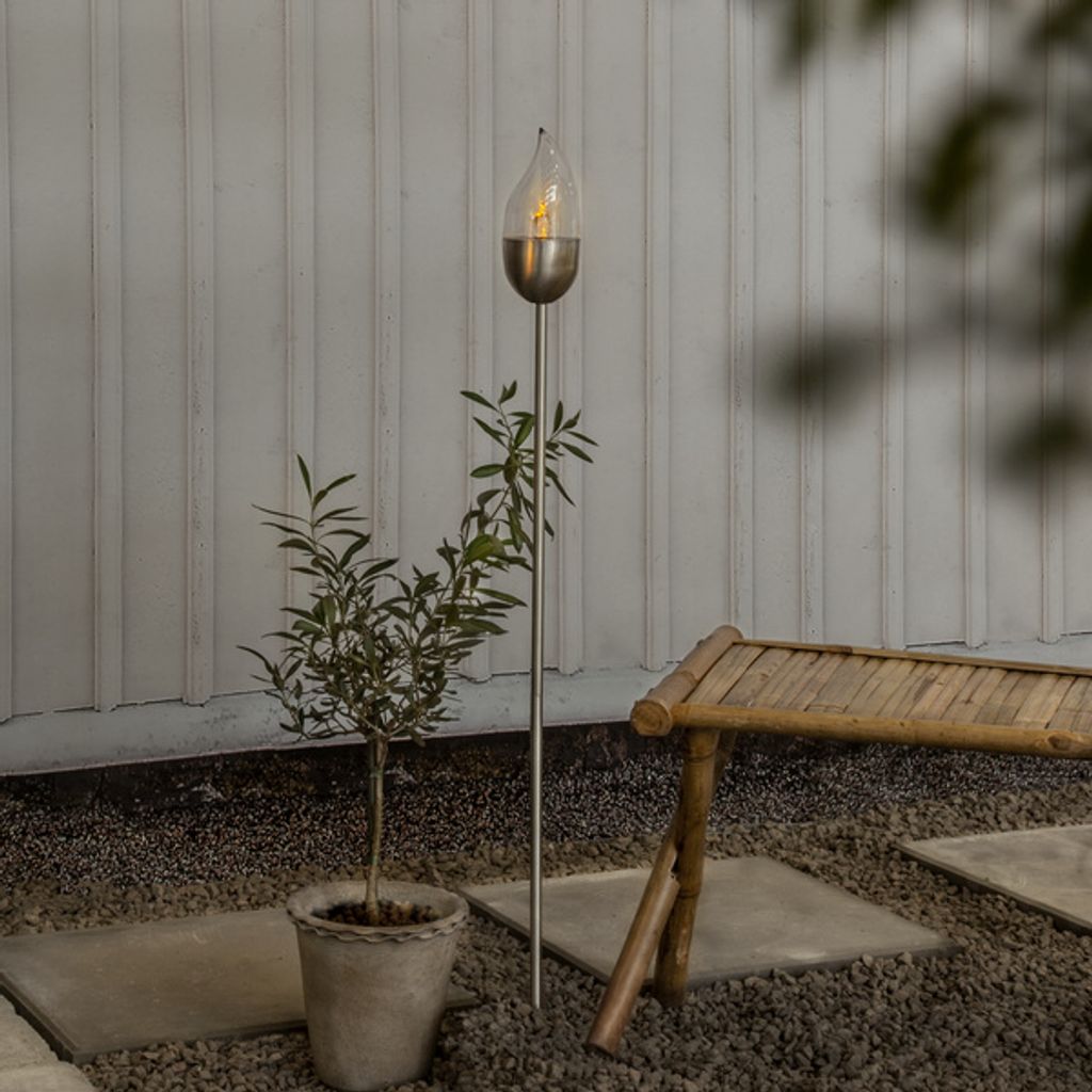 An outdoor setting with a solar-powered LED torch, a potted plant, and a bamboo bench.