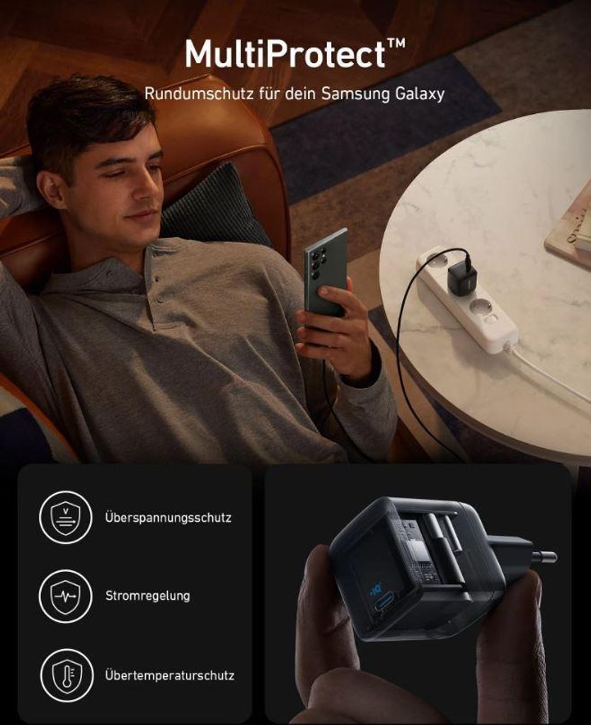 A man is relaxing on a couch while holding a smartphone, with a power strip and charger visible on a table.