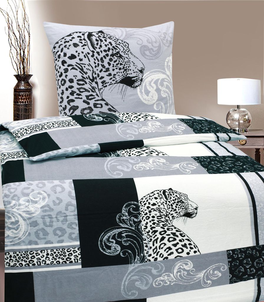 A bed with leopard-print bedding and a pillow, with a vase of branches and a lamp in the background.