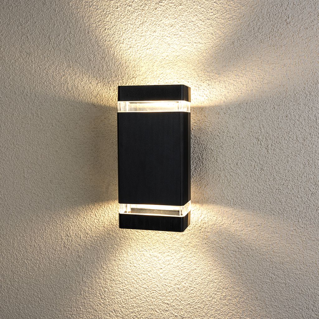 A black rectangular outdoor wall light mounted on a textured wall, emitting light upwards and downwards.