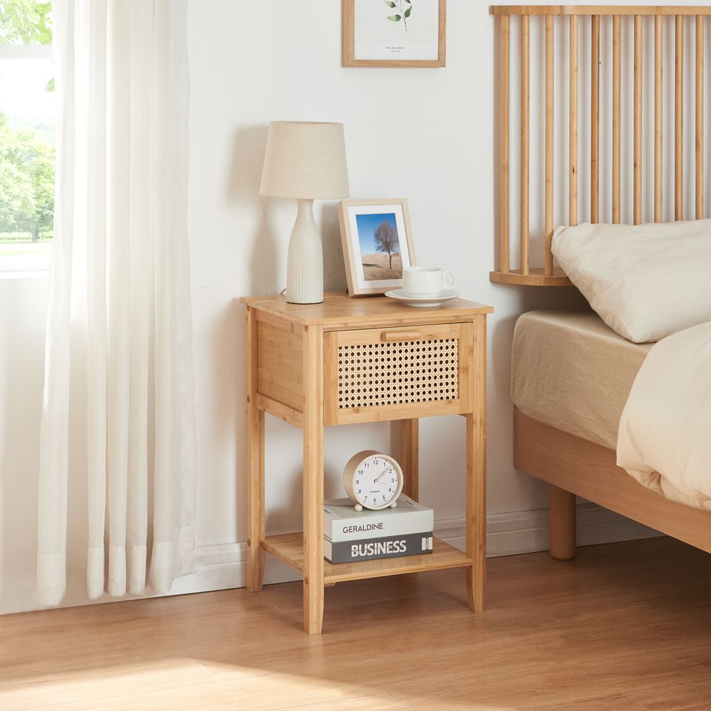 A bedside table next to a bed, with a lamp and picture frame on top.