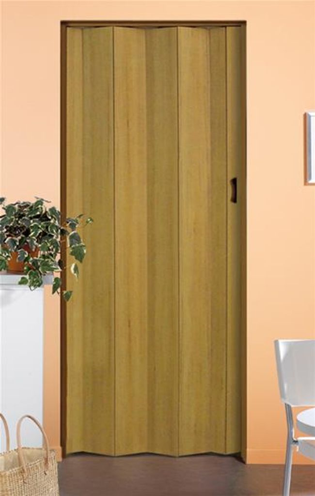 A closed folding door with a wood-like finish, standing in a room with a plant on a shelf to the left and a white chair to the right.