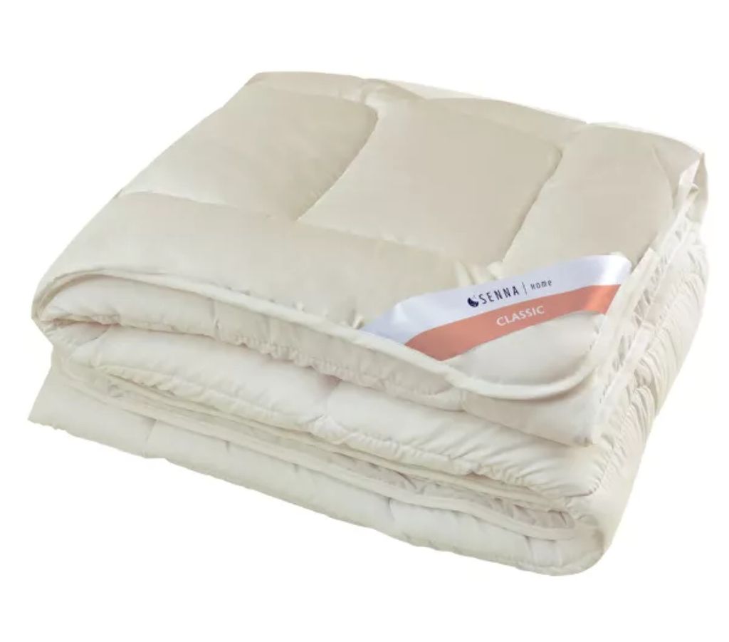 A folded cream-colored duvet or comforter is shown against a white background. A label is attached to the duvet.