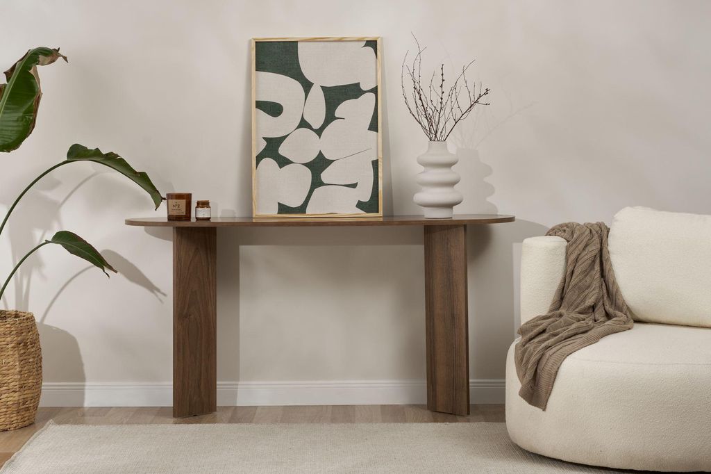 A console table with a piece of art and a vase on it, next to a sofa with a throw blanket.